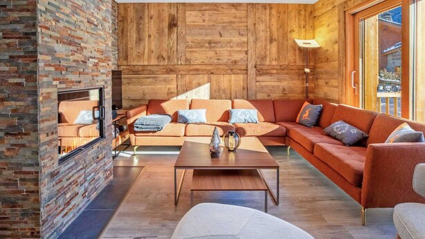 A modern living room with a brick fireplace, wooden walls, a sectional sofa, and a coffee table. - Chalet de l'Olympe A2 (Les Allues)