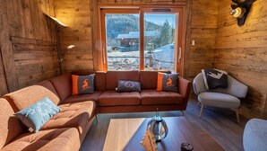 A cozy log cabin interior with a sofa, armchair, and a view of a snowy landscape through a large window. - Chalet de l'Olympe A2 (Les Allues)