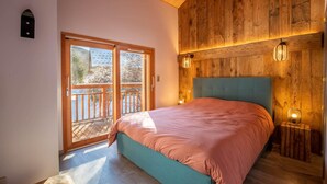 A bedroom with a large bed, wooden walls, and a balcony with a view. - Chalet de l'Olympe A2 (Les Allues)