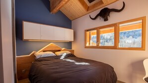 A bedroom with a bed, wooden headboard, a mounted horn, and a window with a snowy view. - Chalet de l'Olympe A2 (Les Allues)