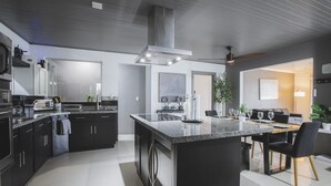 Une cuisine moderne avec des meubles de couleur sombre, un îlot central et un coin repas comprenant une table et des chaises.