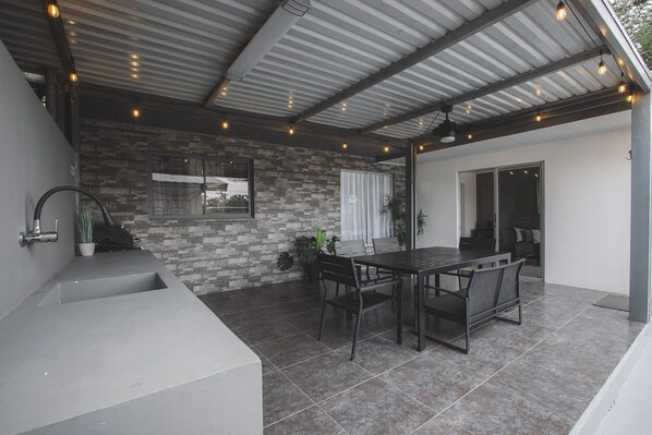 A covered patio with a dining table and chairs, a built-in sink, and a stone wall.