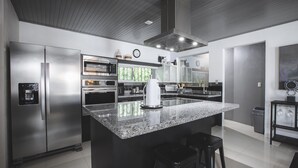 Une cuisine moderne dotée d’appareils électroménagers en acier inoxydable, d’un grand îlot en granit et d’une machine à café.