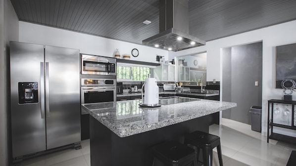 A modern kitchen with stainless steel appliances, a large granite island, and a coffee maker.