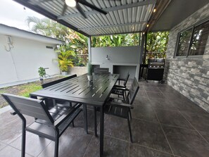 An outdoor patio with a long dining table, chairs, and a grill.