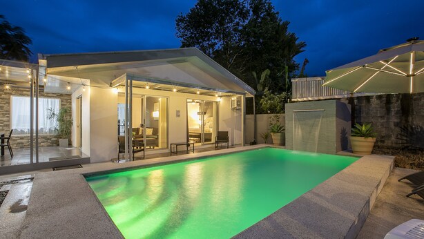 Un espace piscine extérieur moderne, doté d’une structure en verre, de sièges et d’un éclairage d’ambiance.