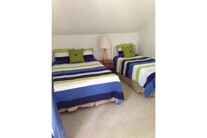 Two single beds with striped bedding, a nightstand, and a lamp sit against a white wall in this cozy space.