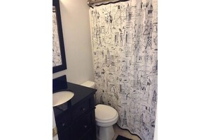 Bathroom features a black vanity with a mirror, a toilet, and a shower curtain with architectural designs.