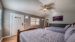 A bedroom with two beds, a ceiling fan, a window with blinds, and a wall-mounted TV.