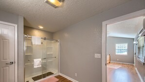 A bathroom with a glass shower enclosure, wooden flooring, and a white door.