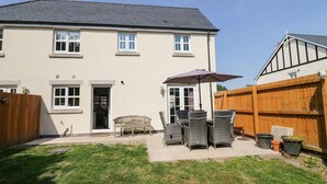 A two-story house with a patio area featuring outdoor furniture and a wooden fence. - Rolo's Retreat (Grange-over-Sands)