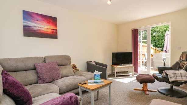 A living room with a sofa, a coffee table, a television, and a view of the outdoors. - Rolo's Retreat (Grange-over-Sands)