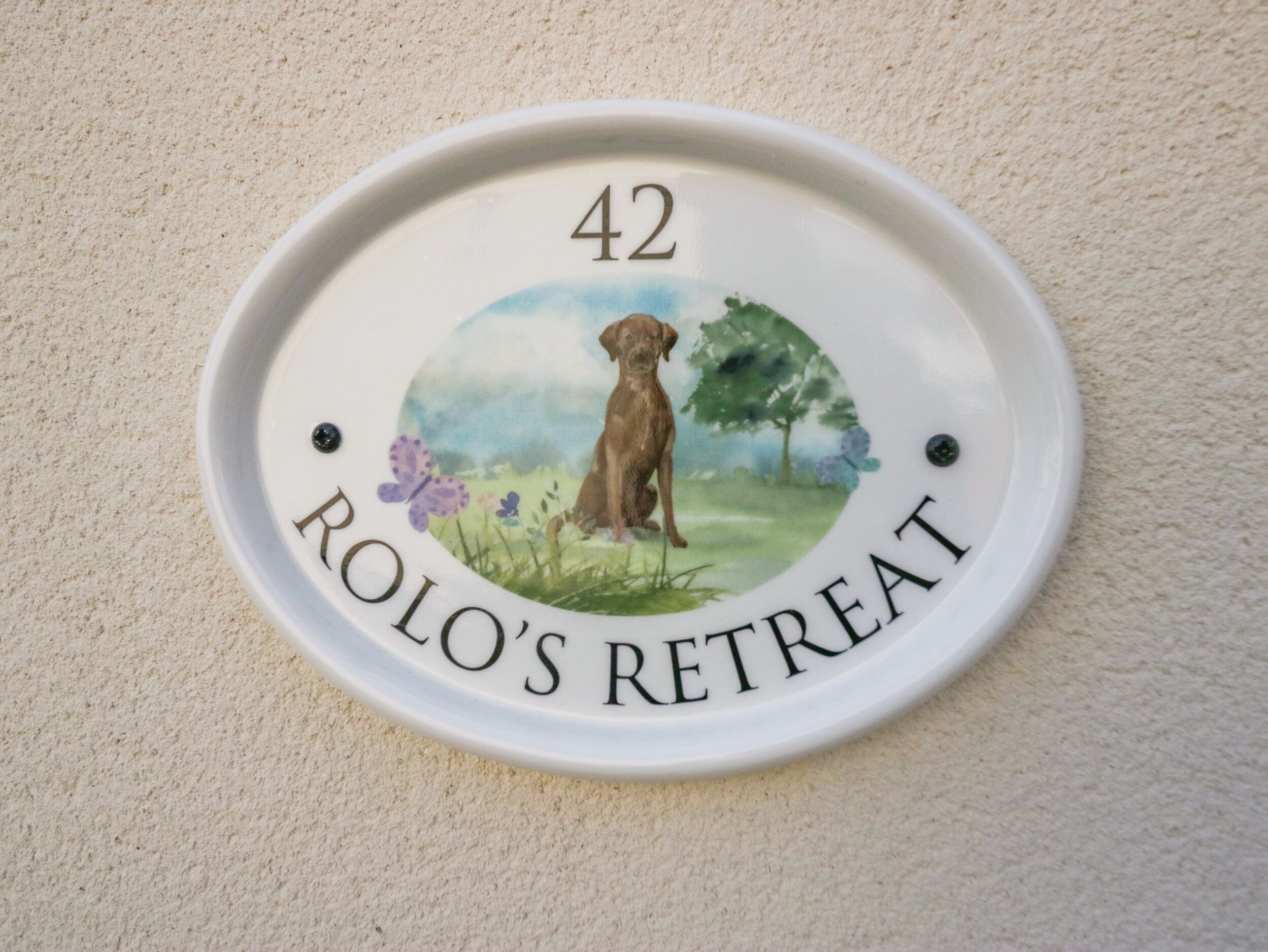 Una placa de número de casa con una ilustración de un perro y el texto 'ROLO'S RETREAT'.