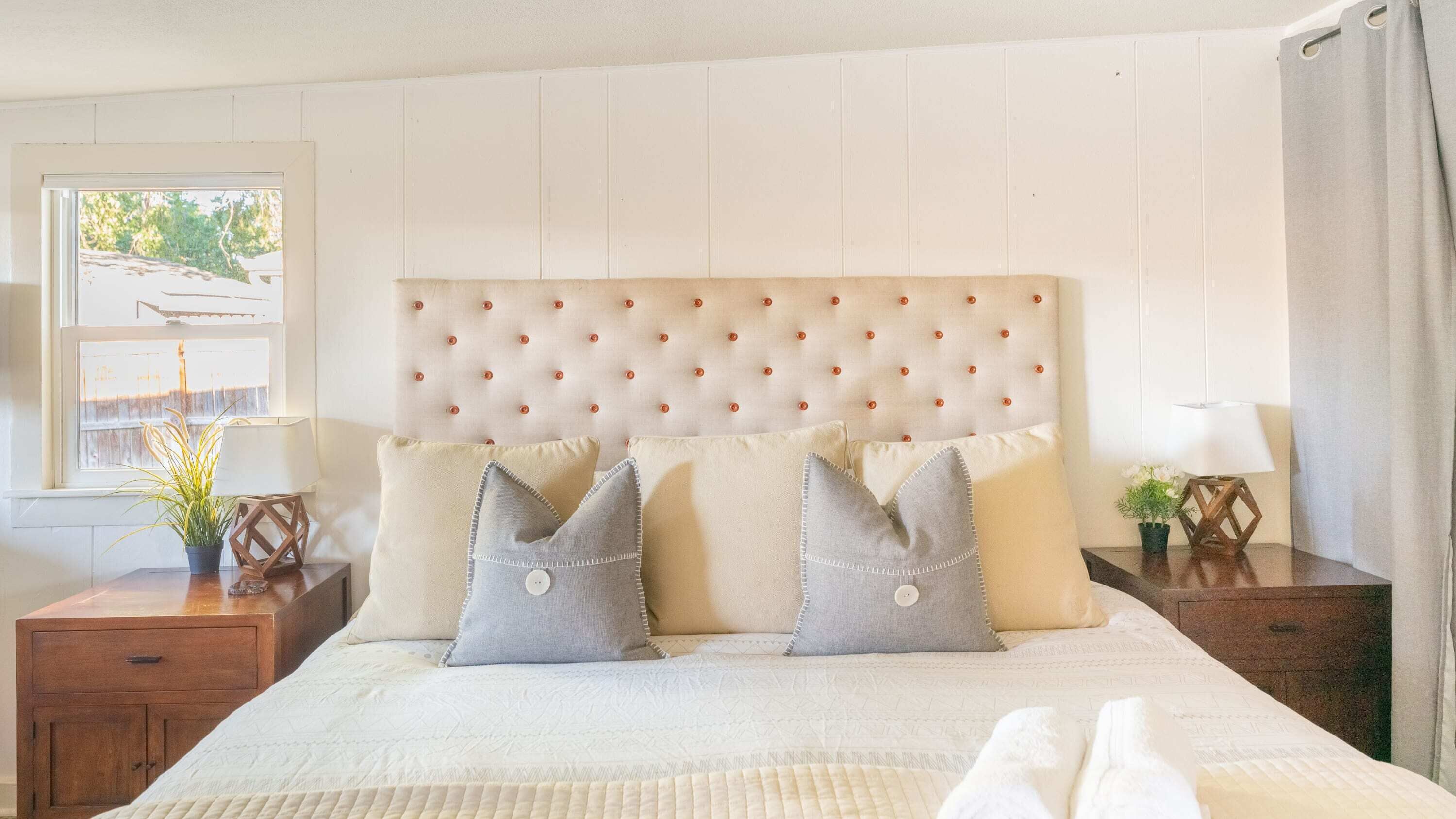 Un lit bien fait, avec une tête de lit capitonnée, deux oreillers gris et une couette blanche.