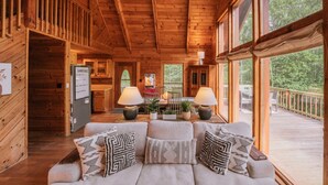 A wooden cabin interior with a sofa, two lamps, a dining table, and a bar area.