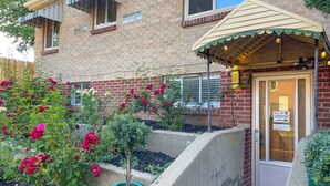 A brick building with a front door, a small porch with string lights, and a garden with red flowers. - Sloans Lake!  Walk to eateries/bars! Free parking! (Denver)