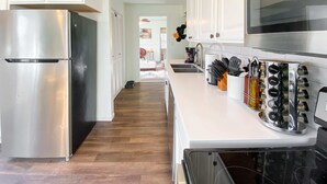 A modern kitchen with stainless steel appliances, a white countertop, and a variety of kitchen utensils and bottles. - Hot Tub, fully fenced, and dog friendly! (Indianapolis)