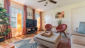 A living room with a flat-screen TV, two red armchairs, a beige sofa, a coffee table, and a large window with curtains. - Hot Tub, fully fenced, and dog friendly! (Indianapolis)