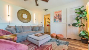 A living room with a grey sofa, a small ottoman, a pink armchair, a round coffee table, and a large mirror on the wall. - Hot Tub, fully fenced, and dog friendly! (Indianapolis)