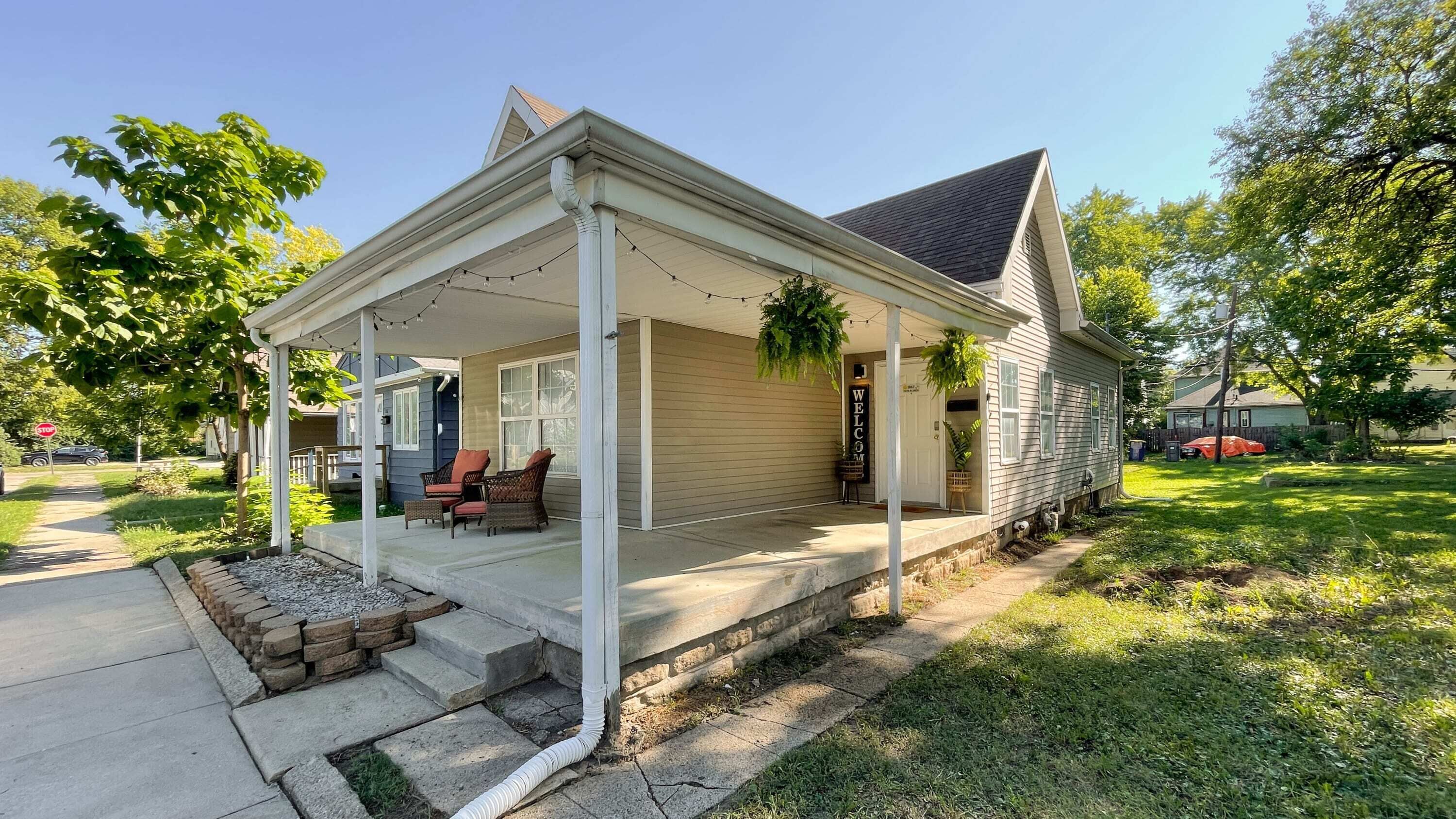 A single-story house with a covered porch, a welcome sign, and outdoor seating.