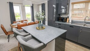 A modern kitchen with grey cabinets, a built-in microwave, and a window with blinds. - Driftwood Lodge (Haverfordwest)