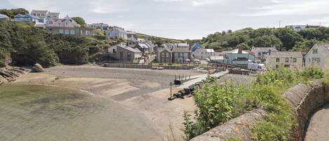 A coastal town with a sandy beach, stone walls, and houses with varying architectural styles.