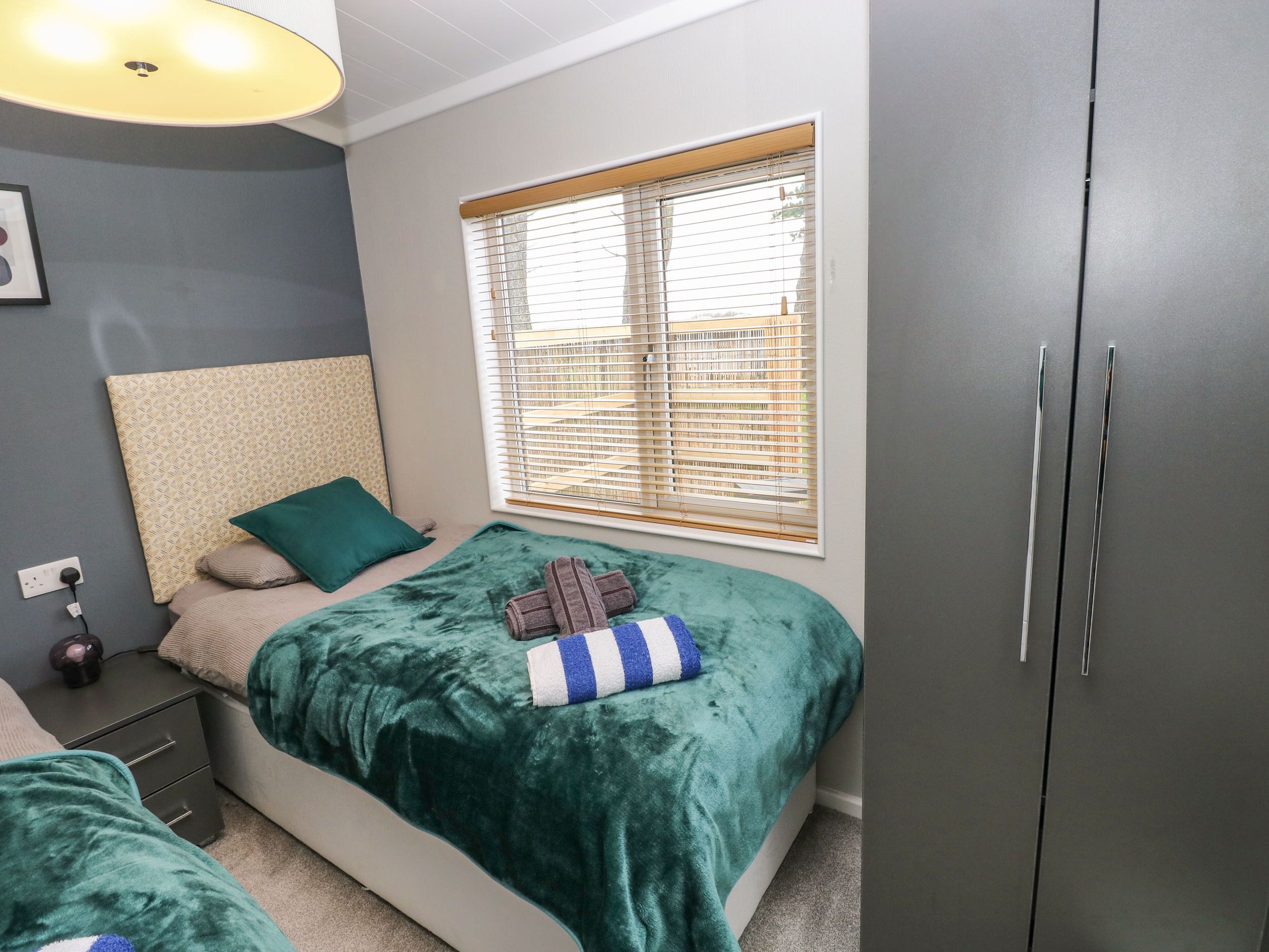 Ein Schlafzimmer mit einem Bett, einem Fenster mit Jalousien, einem Kleiderschrank und einem Nachttisch mit Lampe.