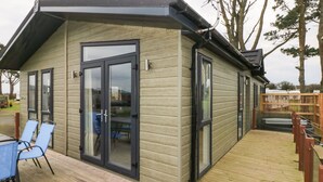 A wooden cabin with a deck, glass doors, and a table with chairs. - Driftwood Lodge (Haverfordwest)