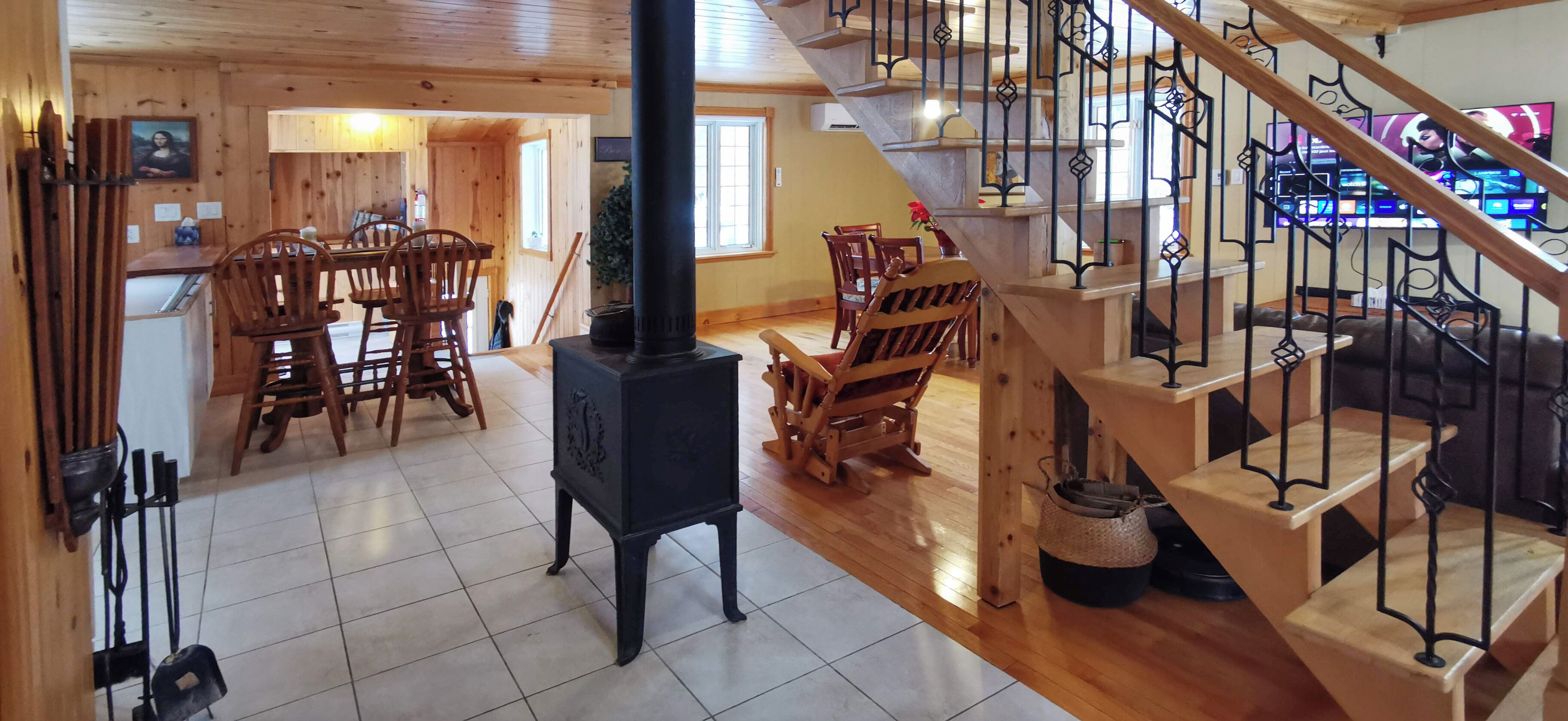 Un intérieur chaleureux avec un coin repas en bois, une cheminée centrale et un escalier doté de rampes en fer forgé.