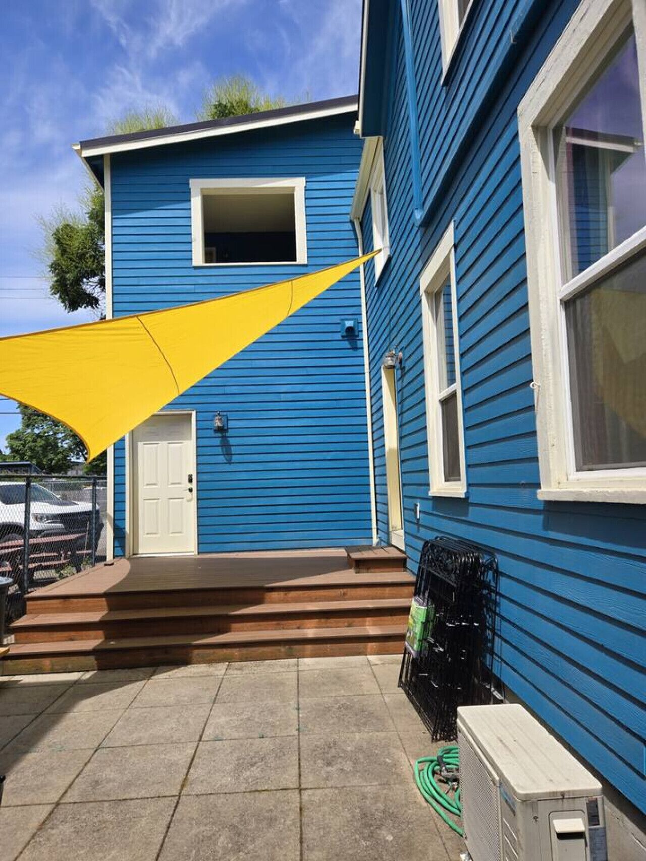 A blue building with a white door, a small porch, and a yellow shade sail.
