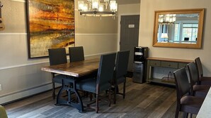 Un comedor con una mesa de madera, seis sillas, una araña, un cuadro abstracto grande y un espejo en la pared.