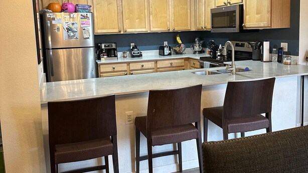 Una cocina moderna con armarios de madera, un refrigerador de acero inoxidable, un microondas y una isla grande con taburetes de bar.