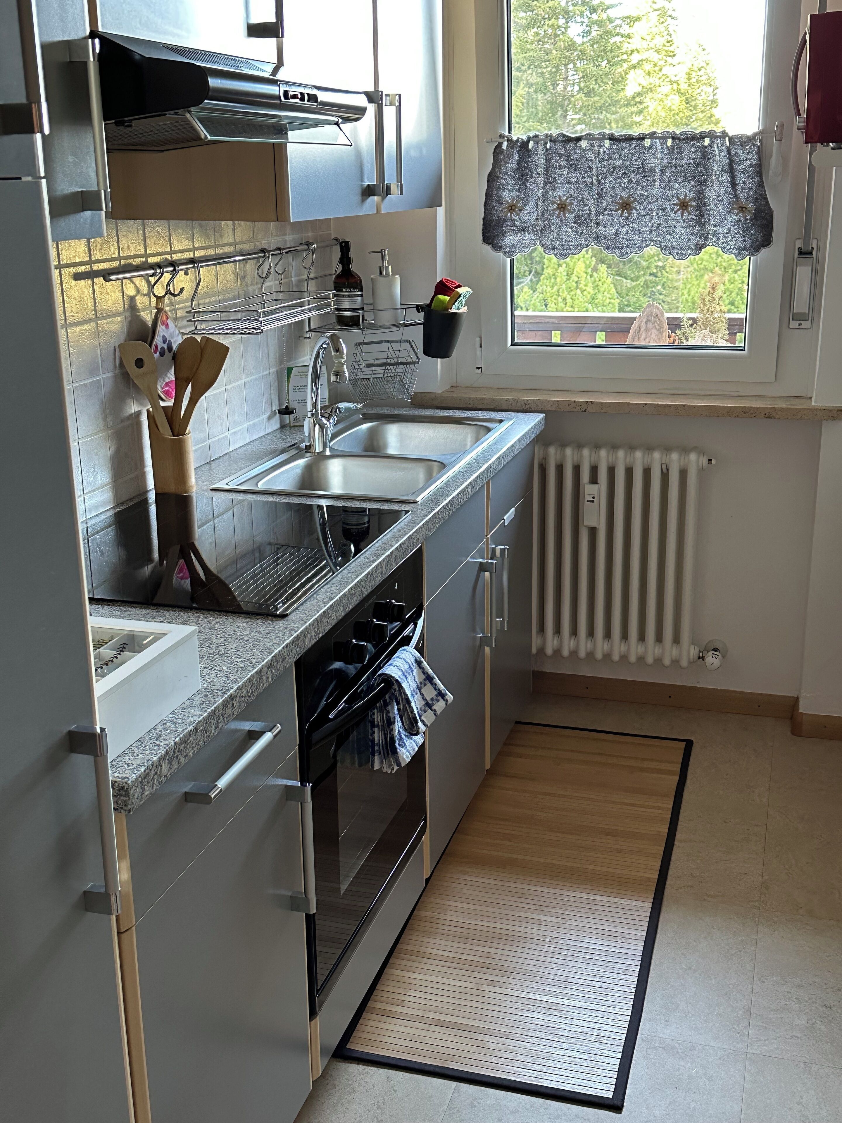 A kitchen with a sink, stove, oven, and a window with a view of greenery.
