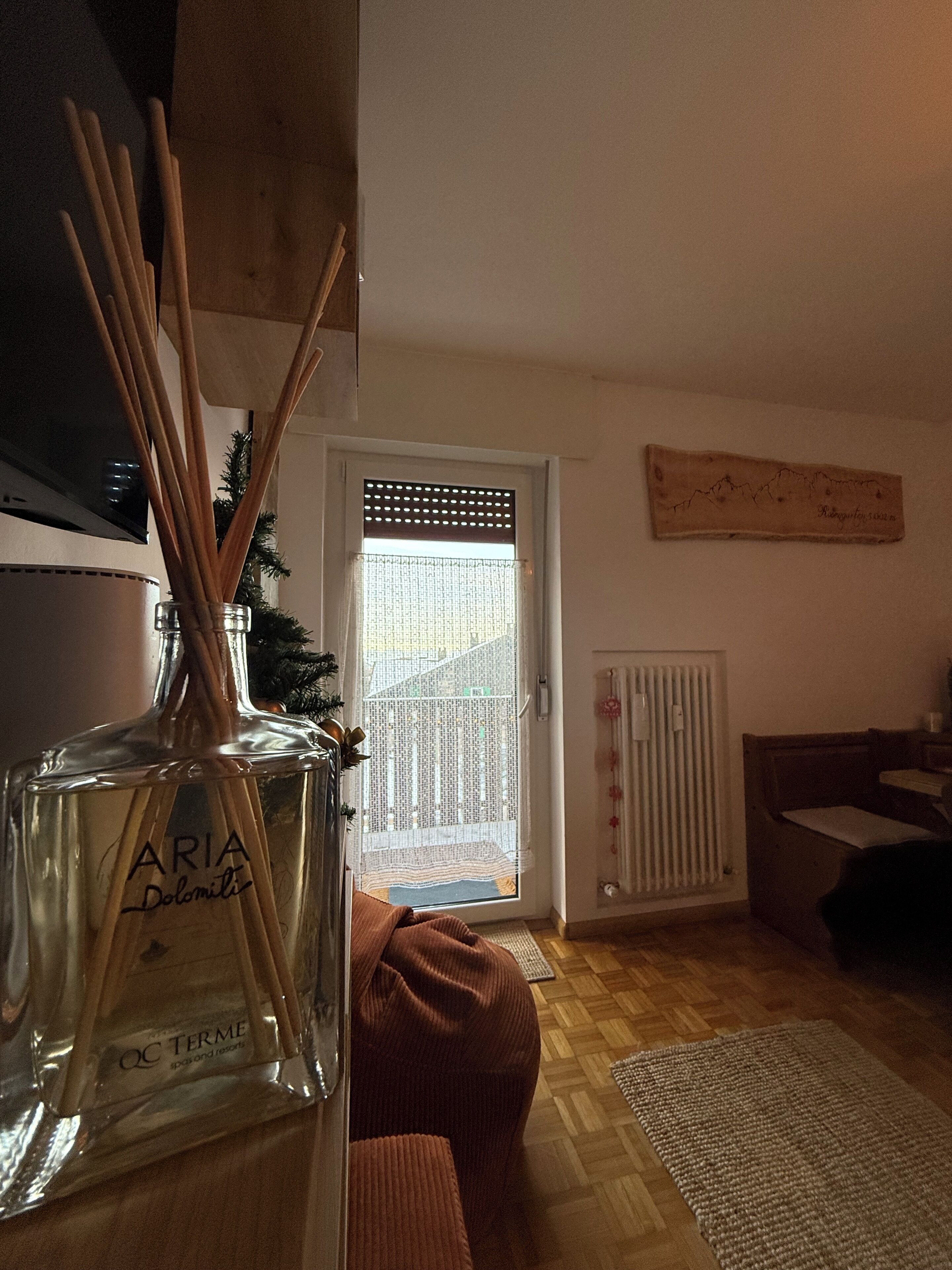 A room with a wooden floor, a brown sofa, a glass bottle of perfume, and a door with a window.