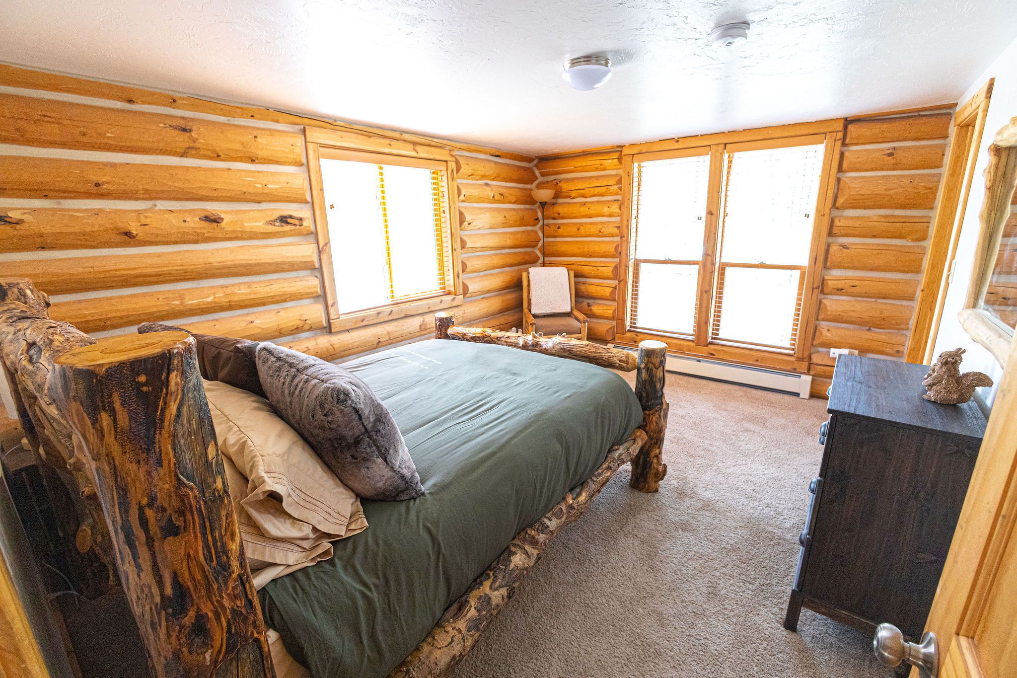 A log cabin bedroom with a bed, a chair, and a dresser.