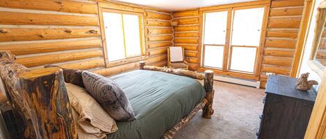 A log cabin bedroom with a bed, a chair, and a dresser.
