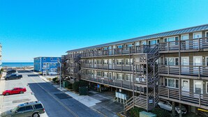 Un hotel de varios pisos con escaleras exteriores y balcones, un estacionamiento y vista al océano.