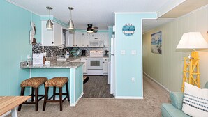 Una cocina compacta con armarios blancos, una isla central con taburetes, un microondas y una estufa.