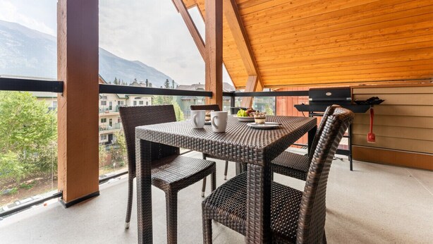A balcony with wicker furniture, a table with a plate of food, and a view of mountains.