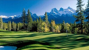 A golf course with a water hazard, trees, and a mountain range in the background.