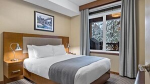 Habitación de hotel con una cama grande, una mesita de noche con lámpara, una ventana con cortinas y un cuadro en la pared.