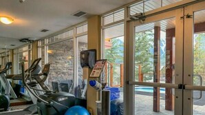 Un gimnasio con cintas de correr, una pelota de ejercicios azul y una piscina visible a través de puertas de vidrio.