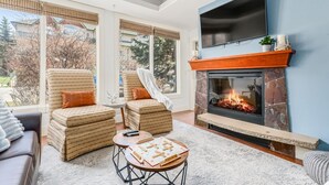 A living room with a fireplace, two armchairs, a sofa, and a coffee table. - AURORA NIGHTS -  COZY LIVING -  SPA, POOL & HOT TUB (Canmore)