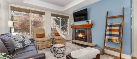 A cozy living room with a fireplace, a sofa, a coffee table, and a TV mounted on the wall.