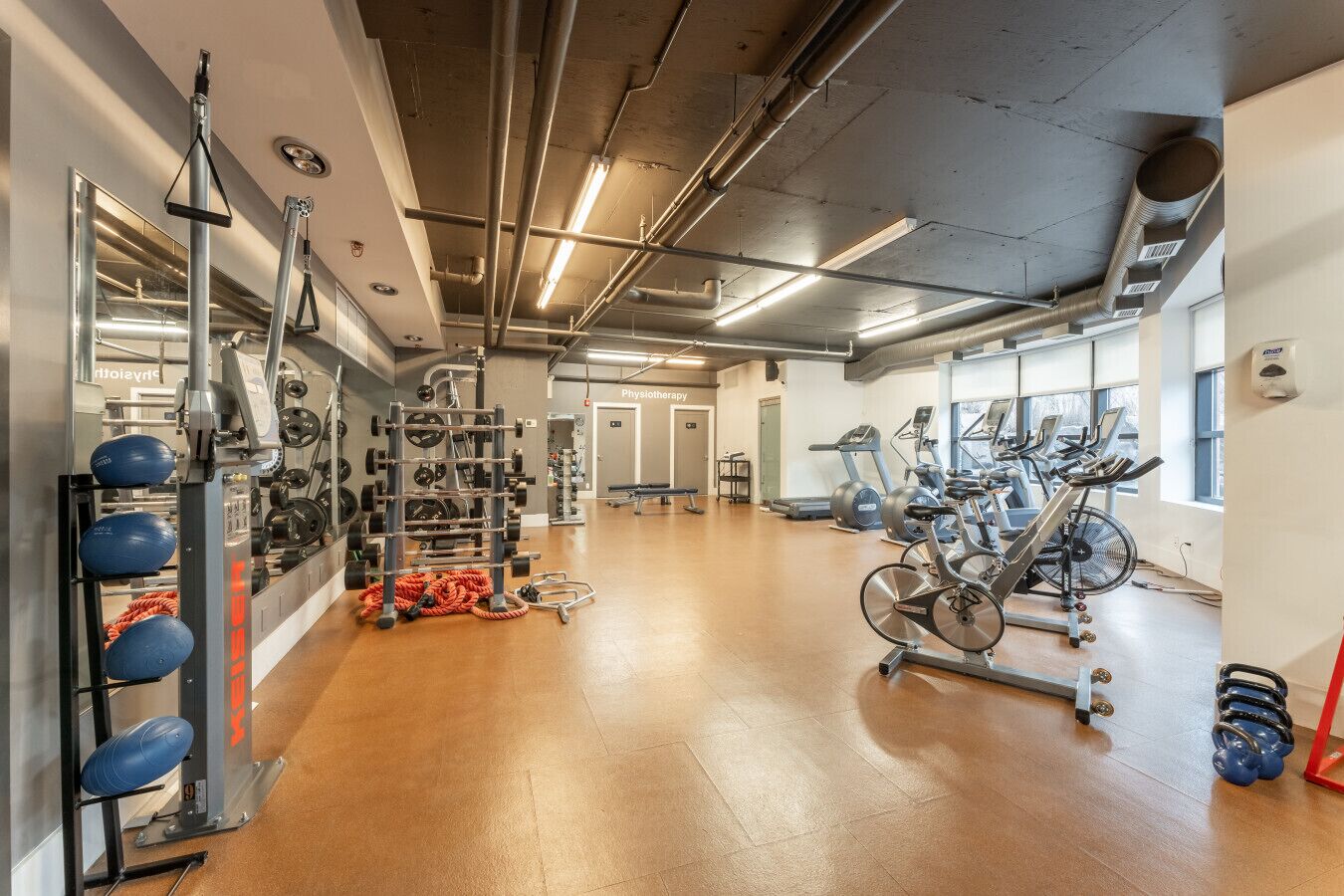 Un gimnasio con equipamiento para levantamiento de pesas, máquinas de cardio y suelo de madera.