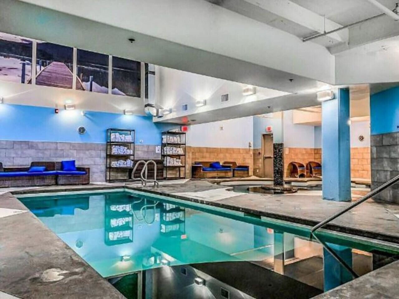 Un espace piscine aux couleurs bleu et blanc, un coin salon avec des coussins bleus et un escalier menant à un niveau supérieur.
