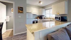 Una cocina moderna con armarios blancos, encimera de granito y microondas integrado.