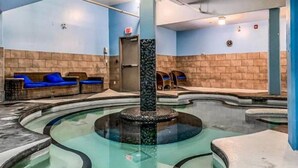 Ein Wellnessbereich mit einer zentralen Whirlwanne, Sitzgelegenheiten und einer Steinsäule.