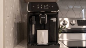 Una cafetera PHILIPS con depósito de agua y una taza blanca sobre una encimera de cocina.