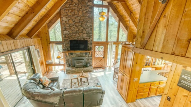 Un interior de cabaña acogedor, con chimenea de piedra, muebles de madera y ventanas amplias.
